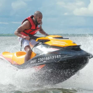 Άντρας με σωσίβιο οδηγεί πορτοκαλί Jet Ski σε γρήγορη ταχύτητα πάνω στο νερό